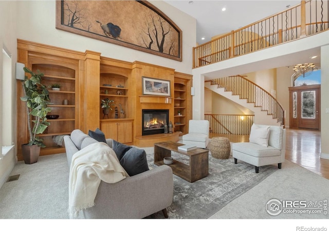 living area featuring a notable chandelier, a towering ceiling, visible vents, stairway, and a glass covered fireplace