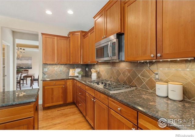 kitchen with stainless steel appliances, brown cabinetry, light wood-style floors, and dark stone countertops