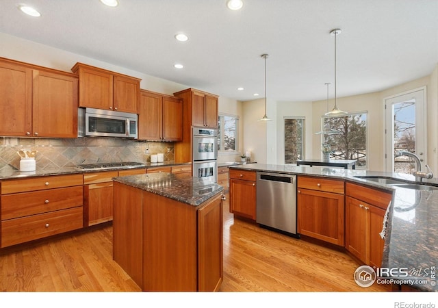 kitchen featuring a center island, pendant lighting, stainless steel appliances, a sink, and dark stone counters