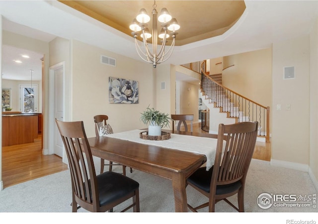 dining room featuring a chandelier, light carpet, visible vents, stairs, and a raised ceiling