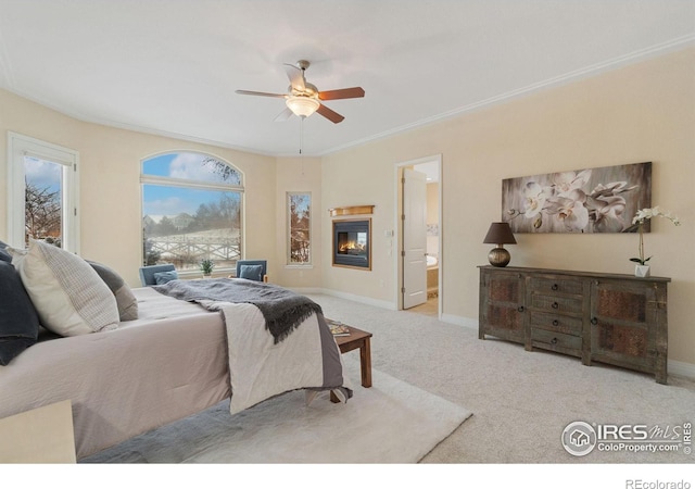 bedroom with crown molding, light colored carpet, a ceiling fan, a glass covered fireplace, and baseboards