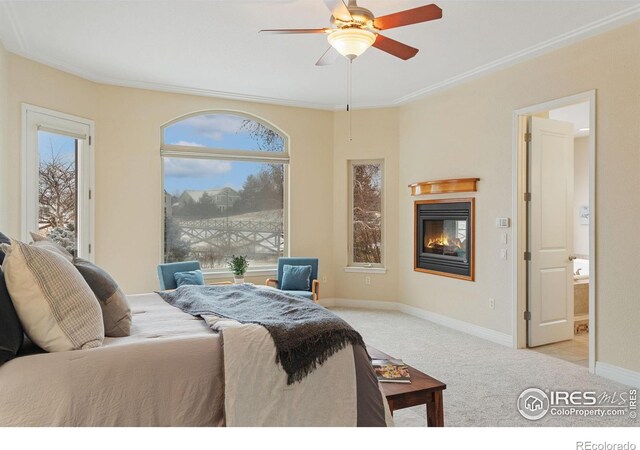 bedroom featuring light colored carpet, a ceiling fan, baseboards, ornamental molding, and a glass covered fireplace