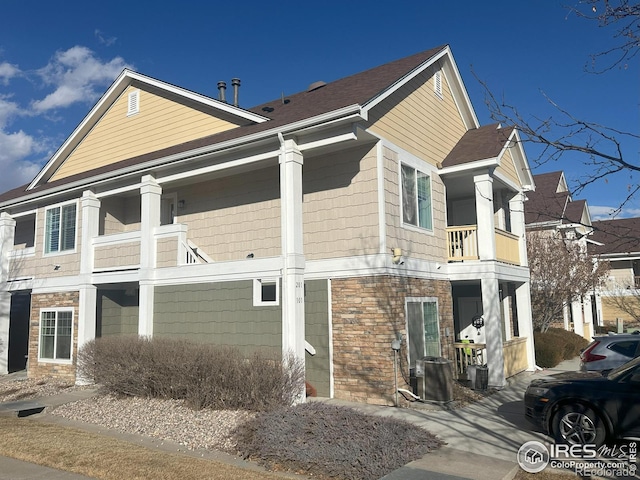 view of home's exterior featuring stone siding, a balcony, and central air condition unit