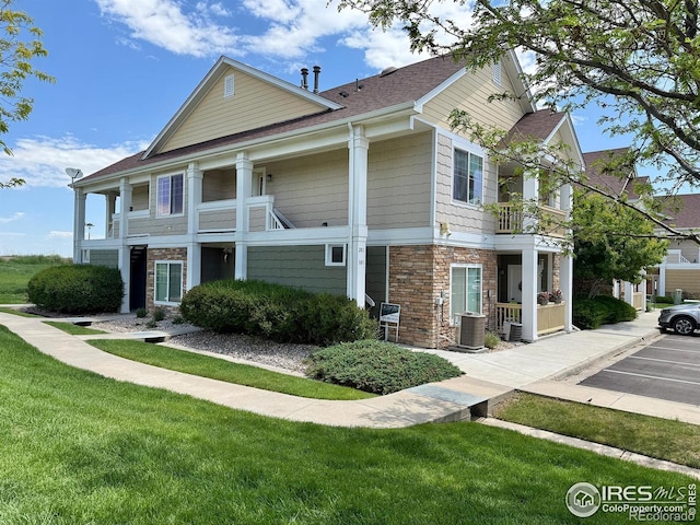 4645 Hahns Peak Dr Unit 201, Loveland, CO 80538 - view of front of home featuring stone siding, a balcony, roof with shingles, a front yard, and uncovered parking