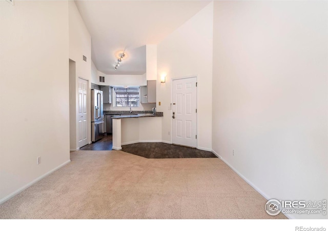 kitchen featuring high vaulted ceiling, a peninsula, high end refrigerator, carpet flooring, and dark countertops