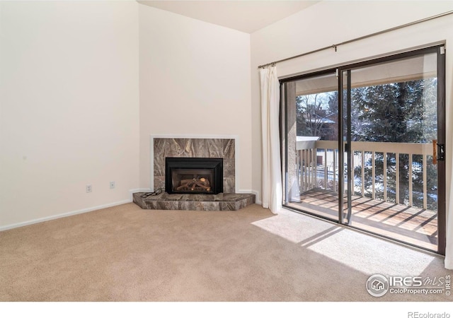 unfurnished living room featuring carpet floors, a fireplace with raised hearth, and baseboards