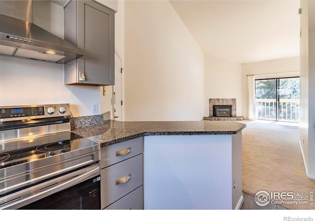 kitchen with light carpet, gray cabinets, stainless steel electric stove, wall chimney exhaust hood, and dark stone countertops