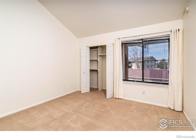 unfurnished bedroom featuring lofted ceiling, a closet, light carpet, and baseboards