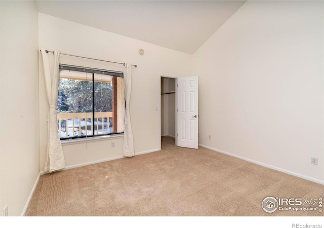 unfurnished bedroom with light carpet, vaulted ceiling, a spacious closet, and baseboards