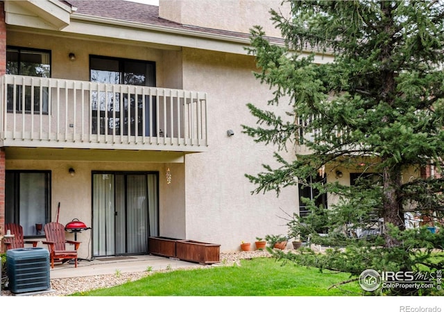 rear view of house featuring stucco siding, central AC, and a balcony