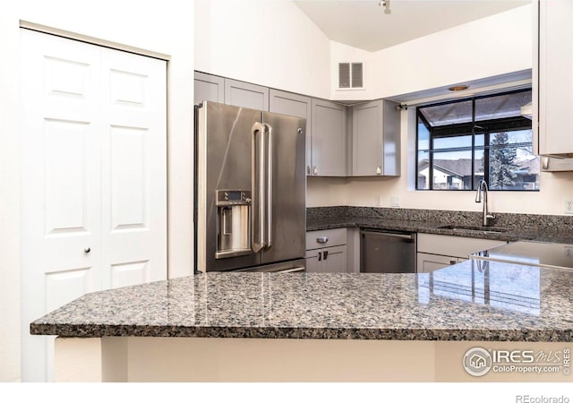 kitchen with a sink, gray cabinets, dark stone countertops, stainless steel appliances, and visible vents