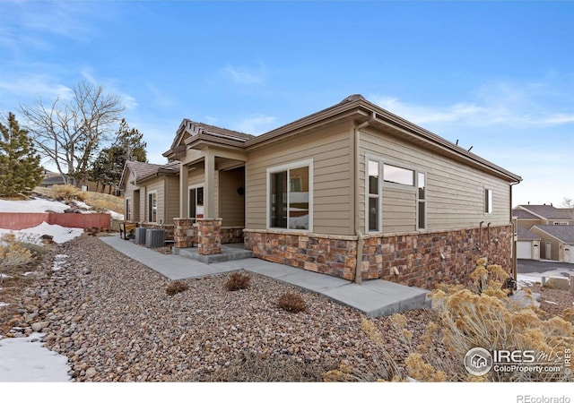 snow covered property with stone siding, a patio, fence, and central air condition unit