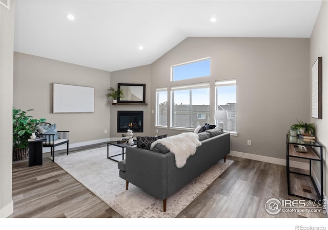 living room featuring high vaulted ceiling, a glass covered fireplace, wood finished floors, and baseboards