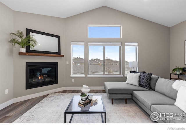 living area with baseboards, vaulted ceiling, wood finished floors, and a glass covered fireplace