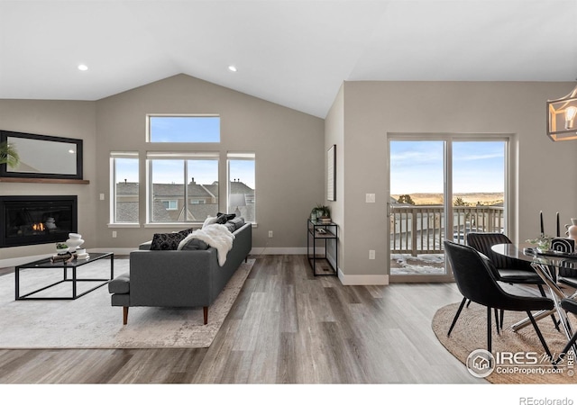 living room featuring high vaulted ceiling, recessed lighting, wood finished floors, baseboards, and a glass covered fireplace