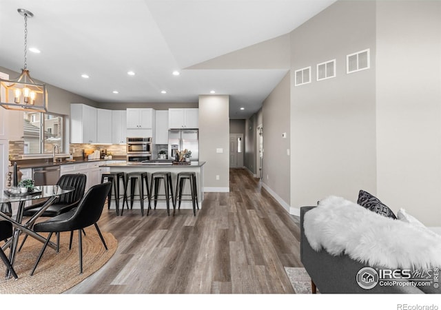 interior space featuring a breakfast bar area, stainless steel appliances, visible vents, white cabinetry, and decorative light fixtures