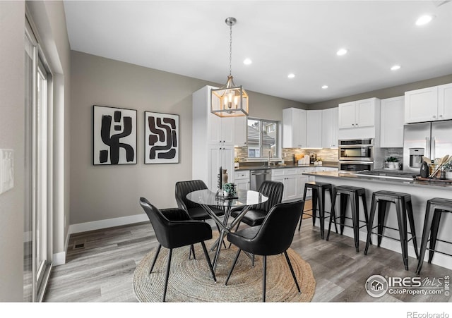 dining room featuring light wood-type flooring, a notable chandelier, baseboards, and recessed lighting