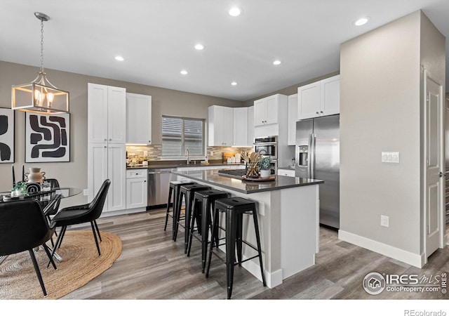 kitchen featuring dark countertops, a kitchen island, stainless steel appliances, a kitchen bar, and white cabinetry