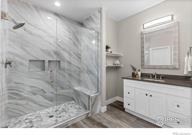 bathroom featuring baseboards, vanity, a marble finish shower, and wood finished floors