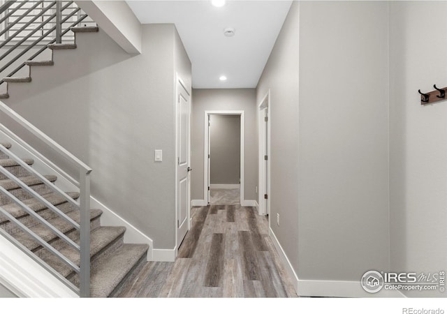 corridor with stairs, recessed lighting, wood finished floors, and baseboards