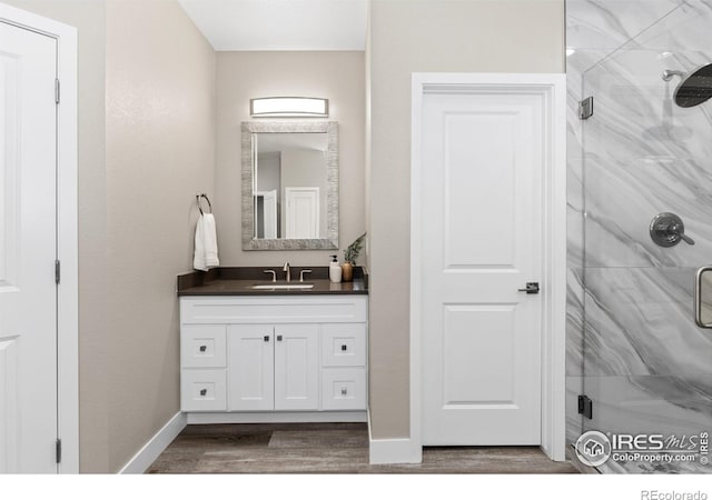 bathroom with wood finished floors, a shower stall, vanity, and baseboards