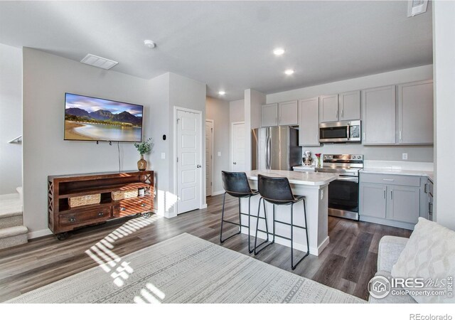 kitchen with a breakfast bar area, gray cabinetry, dark wood-type flooring, a kitchen island, and appliances with stainless steel finishes