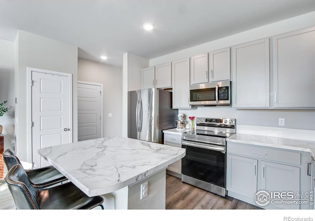 kitchen featuring a kitchen island, a kitchen breakfast bar, dark wood-style flooring, light stone countertops, and stainless steel appliances