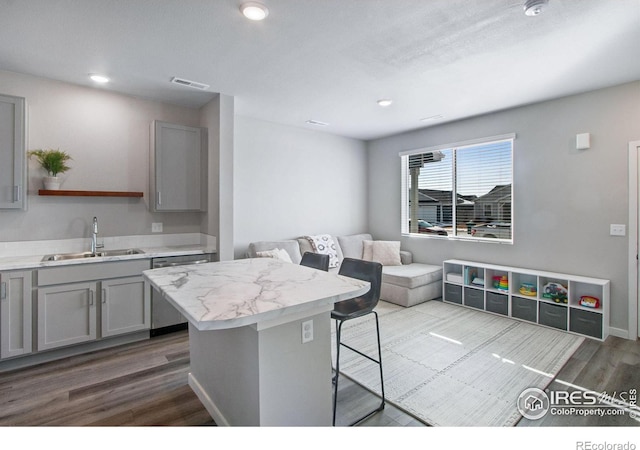 kitchen featuring a kitchen breakfast bar, a sink, gray cabinets, open shelves, and stainless steel dishwasher