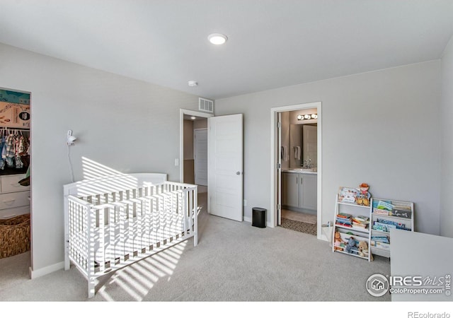 bedroom featuring a crib, visible vents, a sink, and light colored carpet