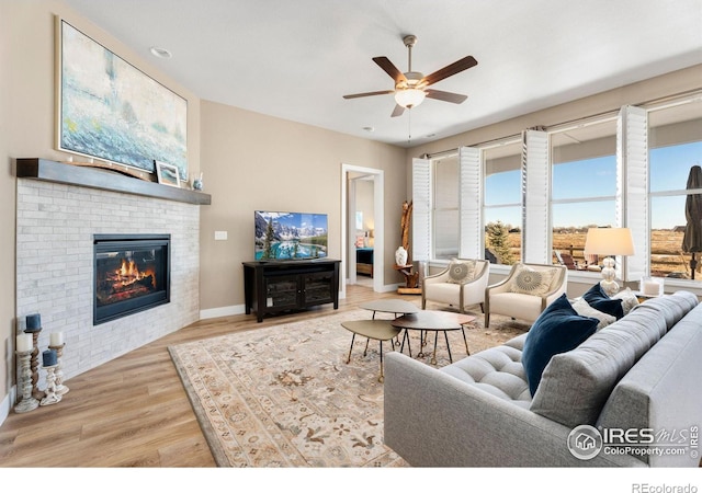 living area featuring ceiling fan, a fireplace, baseboards, and light wood-style floors