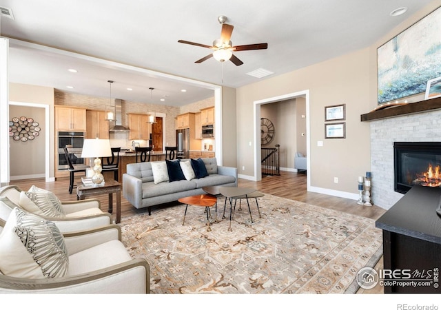 living room with a ceiling fan, visible vents, baseboards, light wood-type flooring, and a glass covered fireplace