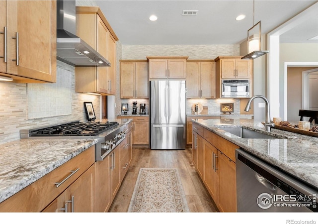 kitchen with visible vents, wall chimney exhaust hood, appliances with stainless steel finishes, light stone counters, and a sink