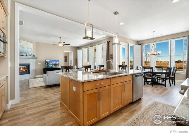 kitchen featuring light stone counters, a kitchen island with sink, a sink, dishwasher, and decorative light fixtures