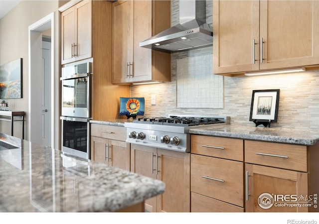 kitchen with stainless steel appliances, backsplash, wall chimney range hood, and light stone countertops