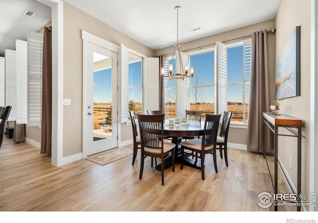 dining area featuring light wood-type flooring, visible vents, a notable chandelier, and baseboards