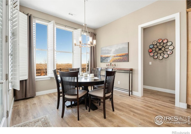 dining room featuring baseboards, visible vents, light wood-style flooring, and an inviting chandelier