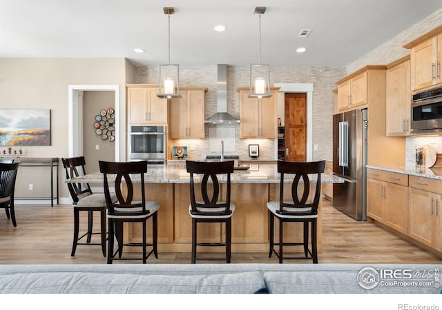 kitchen featuring a center island, decorative light fixtures, light stone countertops, stainless steel appliances, and wall chimney range hood