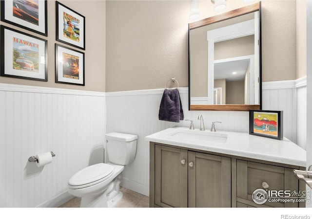 bathroom with a wainscoted wall, vanity, toilet, and tile patterned floors