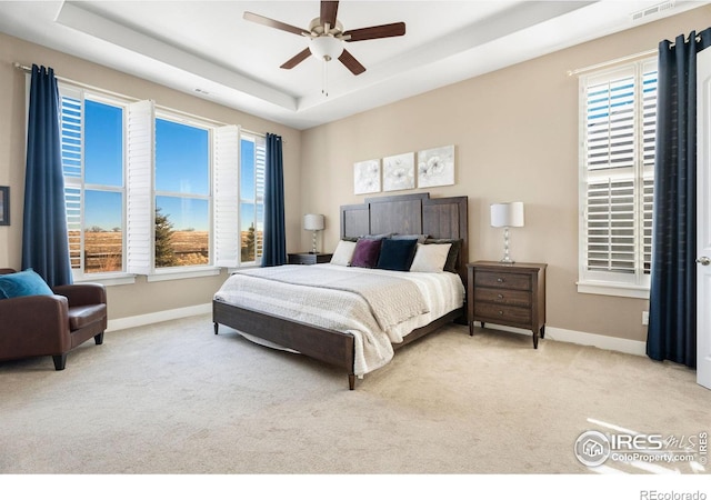 bedroom with light carpet, baseboards, multiple windows, and a tray ceiling