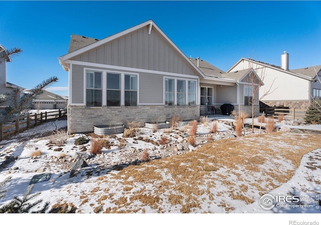 snow covered house with stone siding, board and batten siding, and fence