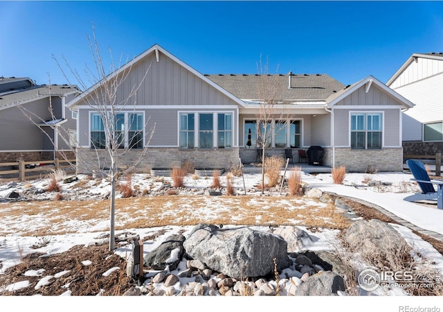 view of front of house featuring stone siding, board and batten siding, fence, and roof with shingles