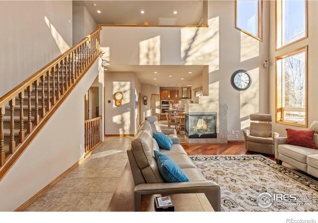 living area with baseboards, a towering ceiling, stairs, a fireplace, and recessed lighting