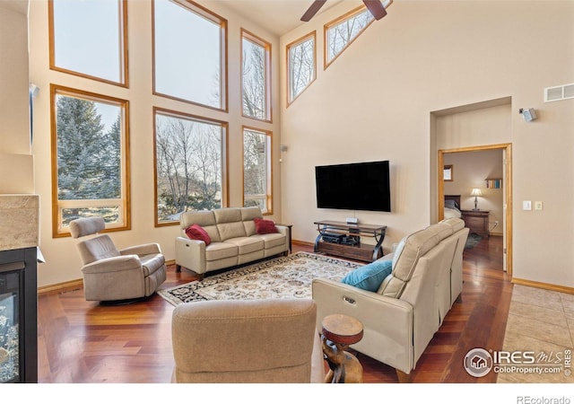 living area with dark wood-type flooring, plenty of natural light, a glass covered fireplace, and visible vents