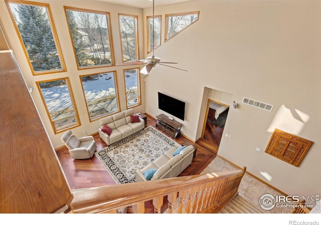 living room with ceiling fan, wood finished floors, a towering ceiling, visible vents, and baseboards