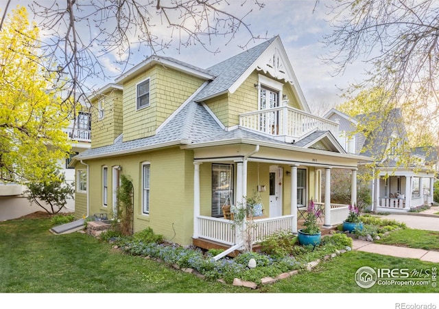 victorian home with a porch, a front lawn, a balcony, and a shingled roof