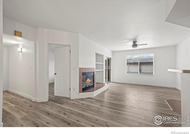 unfurnished living room featuring ceiling fan, built in shelves, a fireplace, and wood finished floors