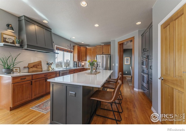 kitchen with stainless steel appliances, a center island, light countertops, brown cabinets, and a kitchen bar