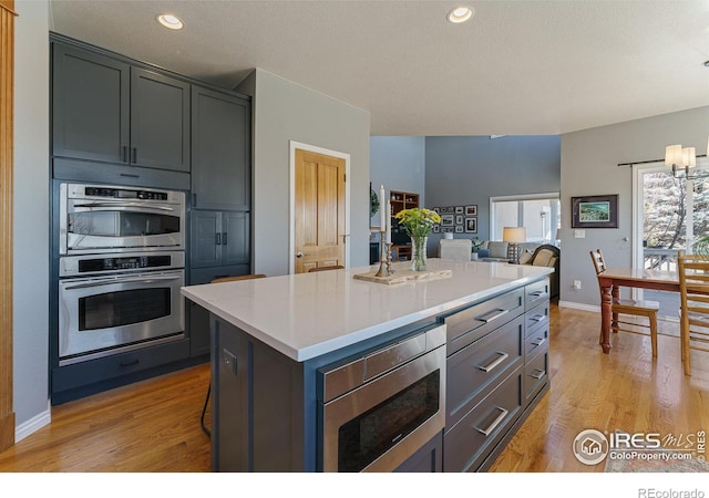 kitchen featuring light wood finished floors, a kitchen island, appliances with stainless steel finishes, a breakfast bar, and light countertops