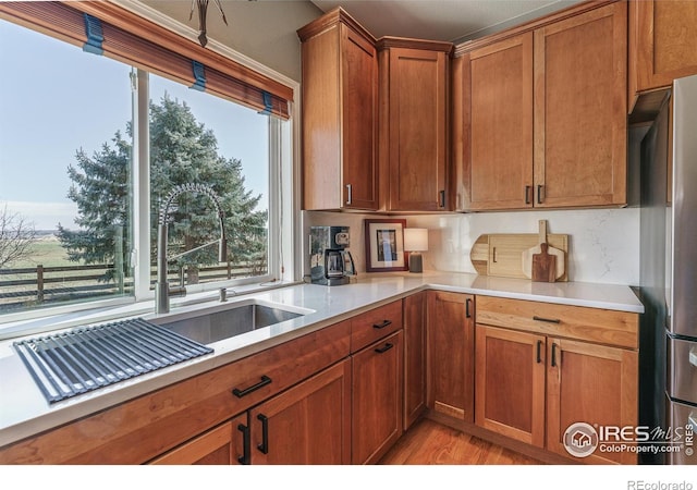 kitchen featuring light wood-style flooring, a sink, light countertops, freestanding refrigerator, and brown cabinets