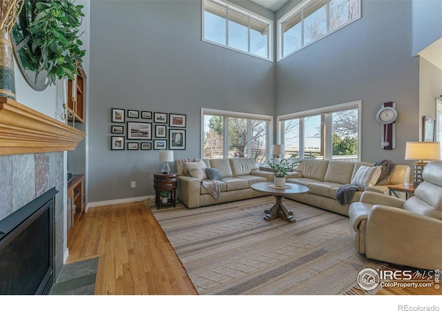 living area with a towering ceiling, baseboards, a tiled fireplace, and wood finished floors